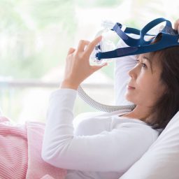 A woman in bed taking off her CPAP machine for sleep apnea.